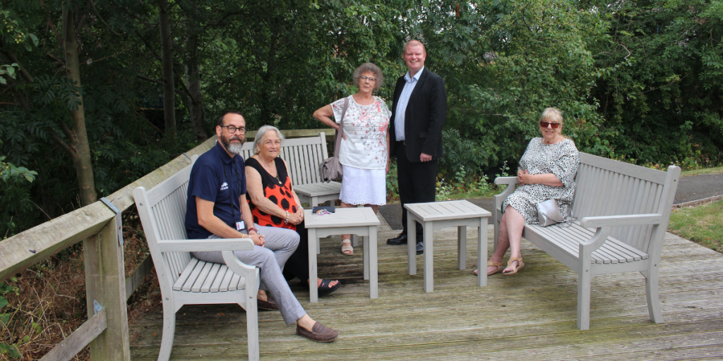 Photo shows Janice Wright, a resident of Riversdale Court retirement housing in Birstall, with Councillor James Poland and fellow residents enjoying the new garden furniture.