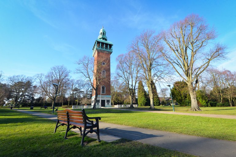 Green space with a bench and a war memorial tower next to severl large trees